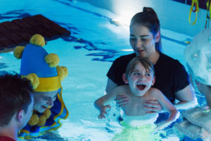 Performers in elaborate costumes interacting with audience members in hydrotherapy pool
