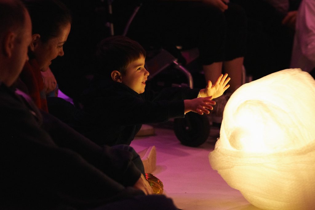 Young boy smiling as he reaches out to touch a big glowing ball of bubble wrap. 