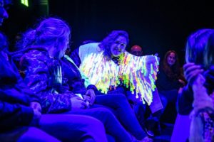 Performer in the audience with a glowing jacket made of little plastic cutlery