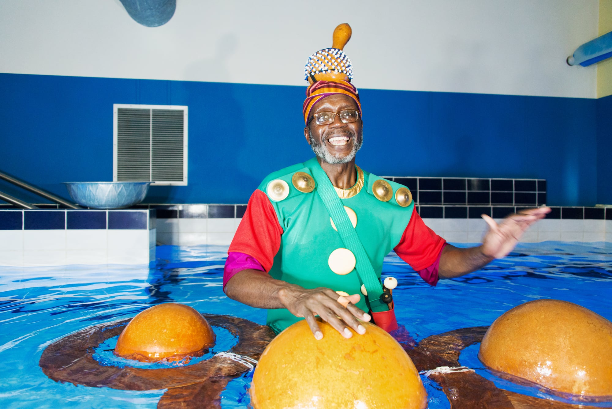 Performer in a swimming pool with round wooden drums