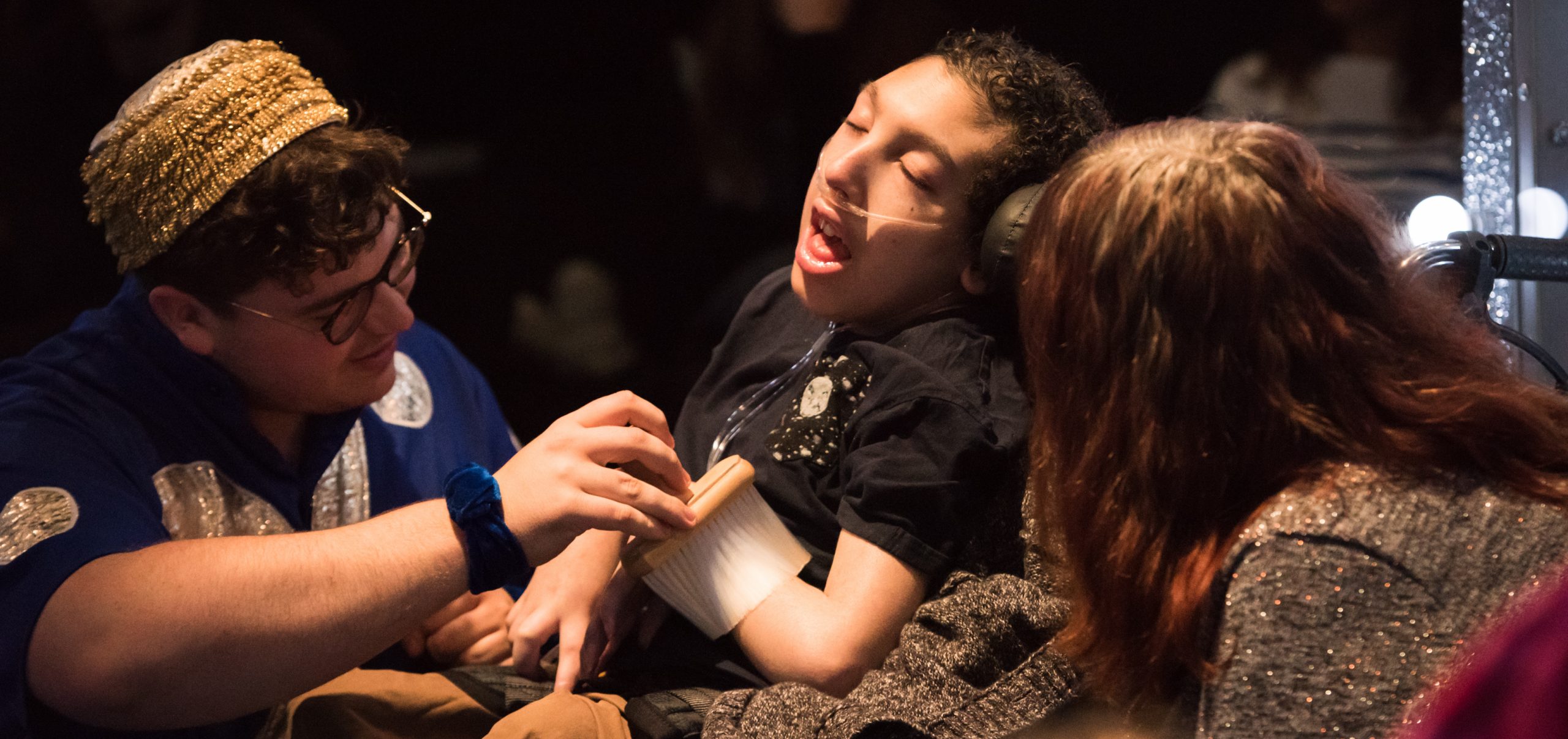 A performer wearing a blue costume with big silver spots runs a soft brush on a young audience member's arm. Photo from Mirror Mirror, credit Neal Houghton