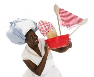 A performer holds a red bowl that has been turned into a ship, with spoons and a checked tablecloth for a sail. A baguette is the sailor. Photo from Baking Time, credit Patrick Baldwin