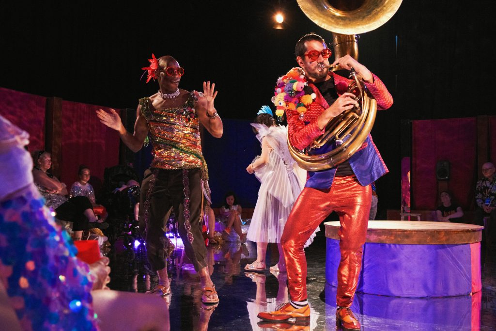 Jamboree band in colourful outfits performing in the centre of the playing space. Photo from Jamboree, credit Suzi Corker