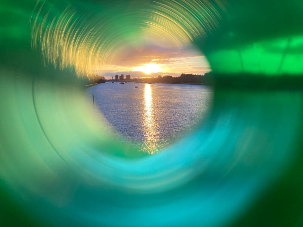 View through a green straw of a sunset over a river with a cityscape. Photo from Something Love, credit Franki Ayres