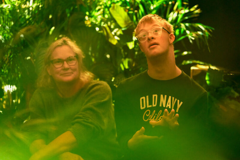 An adult and young person, seen through the green blur of leaves that surround them.