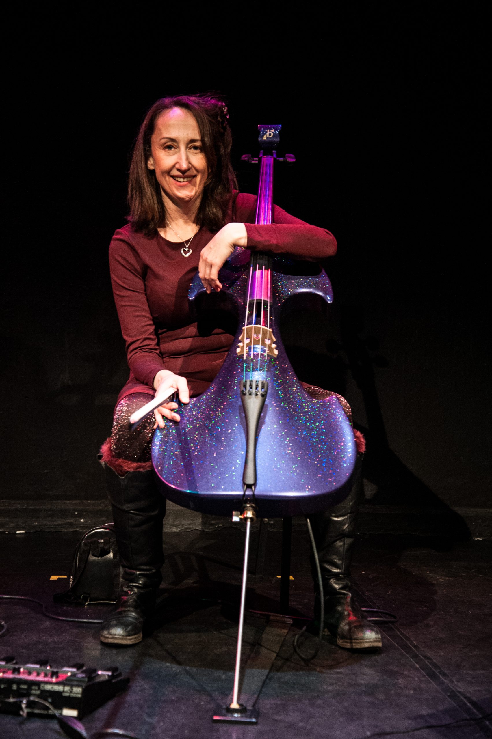 Jo-ann is seated on stage with her cello against a black backdrop. Photo: Oliver Cross