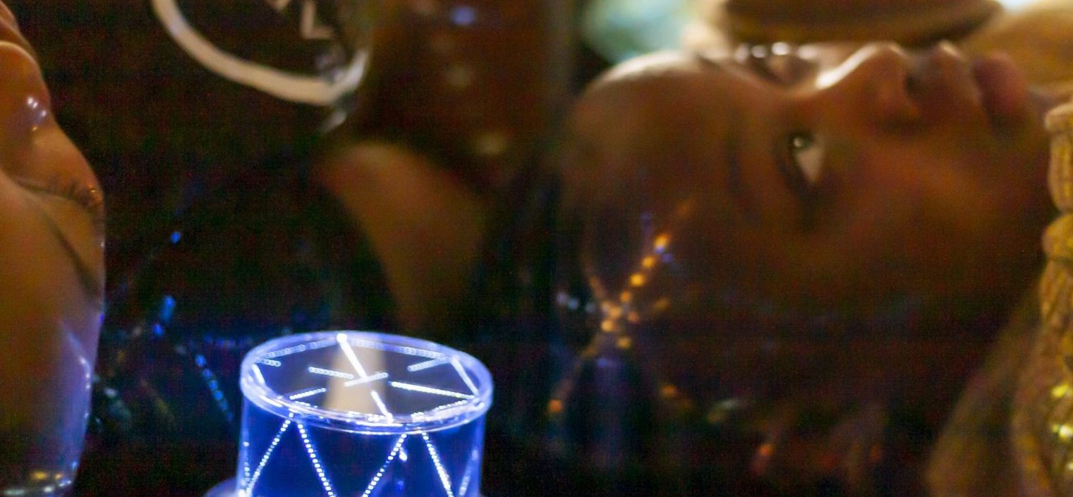 A mum and daughter lie down looking up. There is green gauze material just visible in the background suggesting they are in a tent-like structure. A night light projects dotted coloured lights onto their heads.