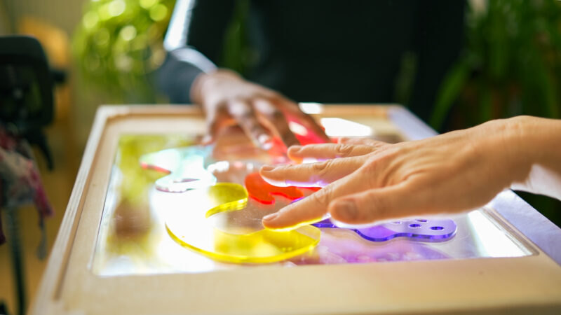 Hands moving colourful perspex shapes over a projector screen