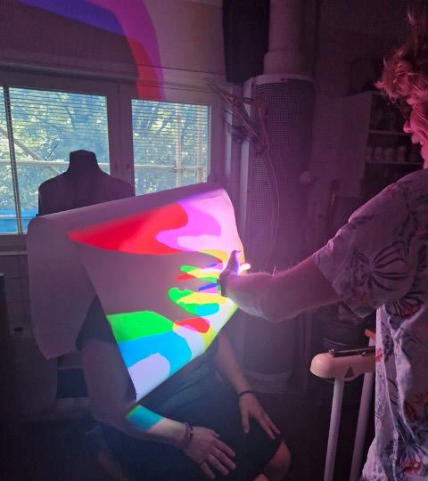 A person creating a colourful shadow of their hand on paper